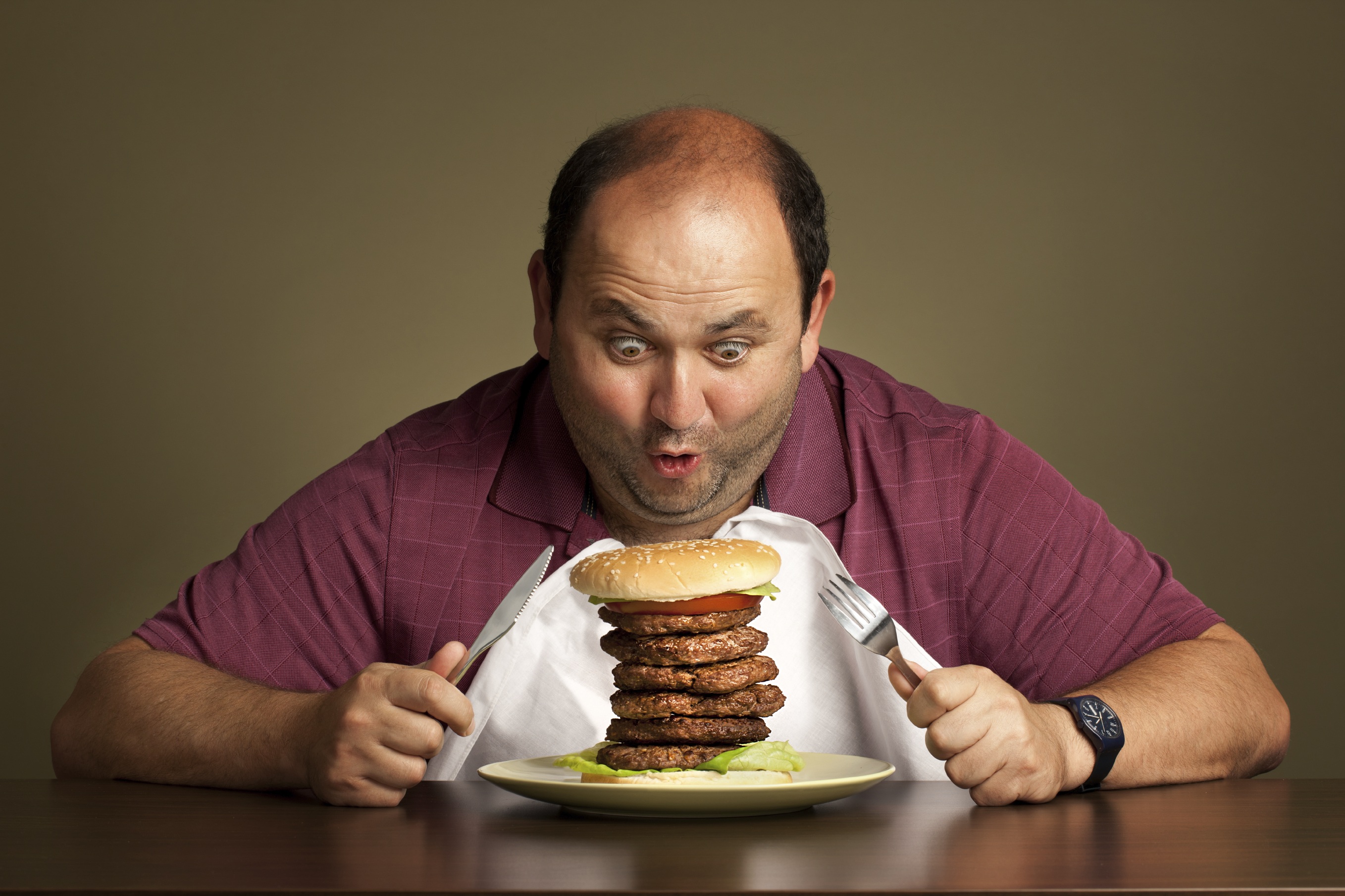 Ешь и толстым становишься. Люди за едой. Мужчина ест гамбургер. Человек ест бургер. Человек ест за столом.